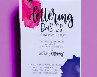 May include: A white booklet with the title "Lettering Basics - The Lowercase Letters -" and a pink and purple watercolor background. The booklet is a lettering practice workbook by Carissa Sliwinski of Positively Lettering. It includes a 41 page guide of tips and techniques to help you learn the art of lettering.