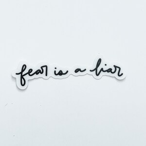 May include: Black and white handwritten text on a white background that reads "fear is a liar".