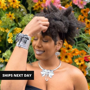May include: Silver-toned elephant jewelry set, including a cuff bracelet, necklace, and earrings. The cuff bracelet features a detailed elephant design with black accents. The necklace has a matching elephant pendant, and the earrings are small elephant shapes.