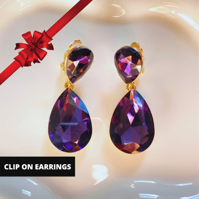 May include: A pair of clip-on earrings with two teardrop-shaped purple crystals on each earring.