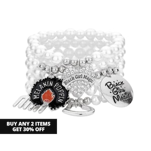 May include: A multi-strand white faux pearl bracelet featuring silver-toned charms. The charms include a black afro pick with the text Melanin Poppin, a heart-shaped charm with clear rhinestones and the text Black Girl Magic, and a round silver disc.