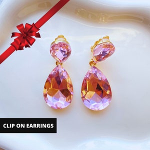 May include: A pair of clip-on earrings with a teardrop-shaped pink crystal and a smaller round pink crystal. The earrings are gold-toned.
