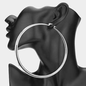 May include: A pair of large, silver hoop earrings. The earrings are displayed on a black mannequin head. The hoops are round and have a shiny, metallic finish. The earrings are a classic accessory.