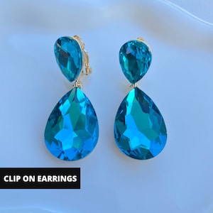 May include: A pair of clip-on earrings with two teardrop-shaped turquoise blue crystals on each earring.