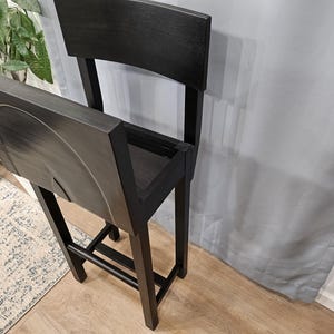 May include: A black wooden chair with a storage compartment in the back. The chair is folded down and the storage compartment is open.