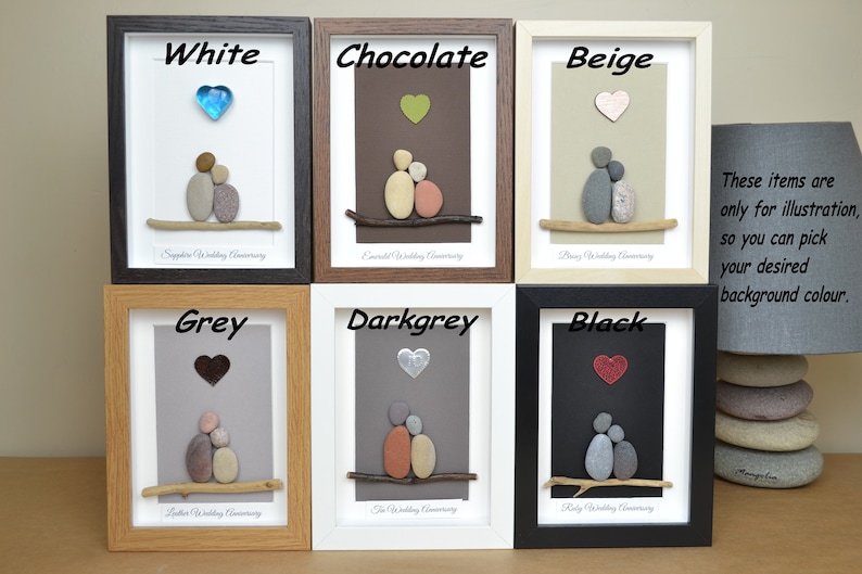 May include: Six framed pebble art pieces depicting a couple sitting on a branch with a heart above them. The frames are in various colors: white, chocolate, beige, grey, dark grey, and black. The text below each piece indicates the wedding anniversary represented. The text "These items are only for illustration, so you can pick your desired background colour." is visible in the bottom right corner.