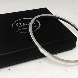 May include: A silver bangle bracelet in a black velvet box with the text "Stoon Handmade Jewellery" on the box.