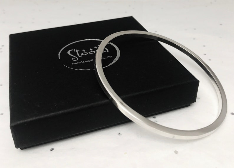 May include: A silver bangle bracelet in a black velvet box with the text "Stoon Handmade Jewellery" on the box.