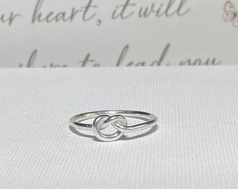 May include: A silver knot ring with a simple design. The ring is made of a single piece of wire that is twisted into a knot shape.