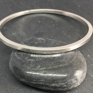 May include: A simple silver bangle bracelet with a flat, polished finish.