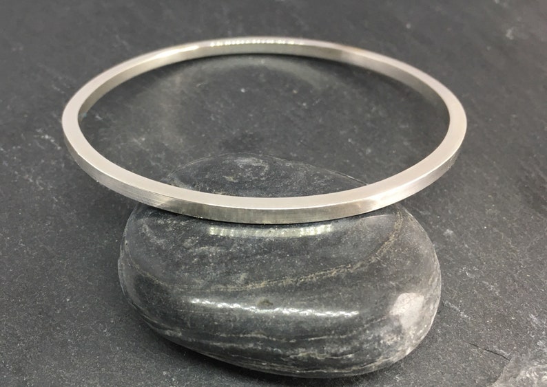 May include: A simple silver bangle bracelet with a flat, polished finish.