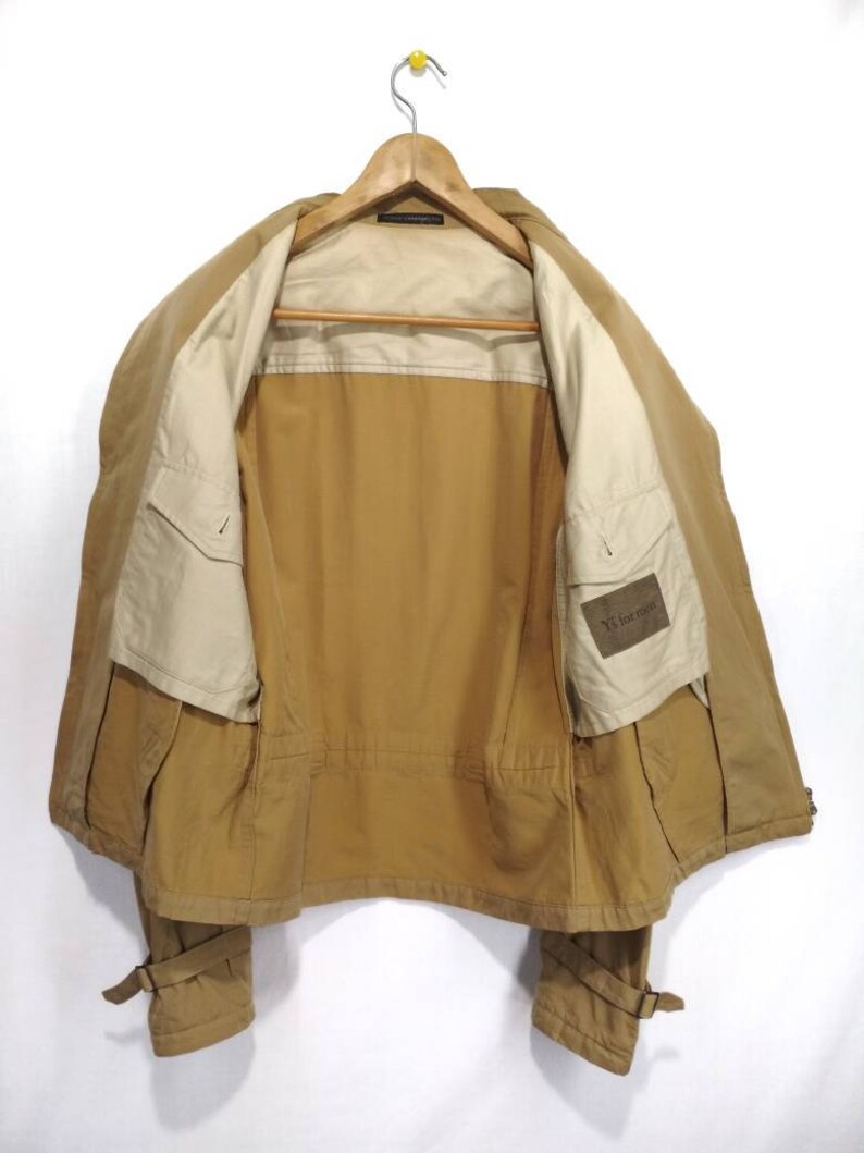 May include: A brown jacket with a beige lining and a small pocket on the left side. The jacket has a zipper closure and two pockets on the front. The jacket has a label on the inside that says "Y's for men".