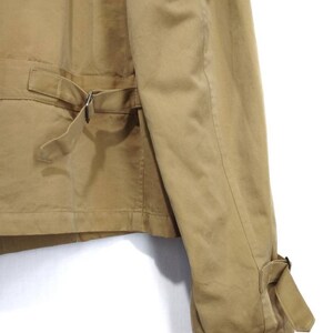 May include: A tan utility jacket with a belt and buckle closure. The jacket has a long sleeve with a buttoned cuff.