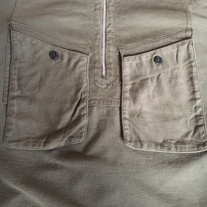 May include: A green, long-sleeved shirt with a zipper closure and two large pockets on the front. The pockets have a flap and a button closure.