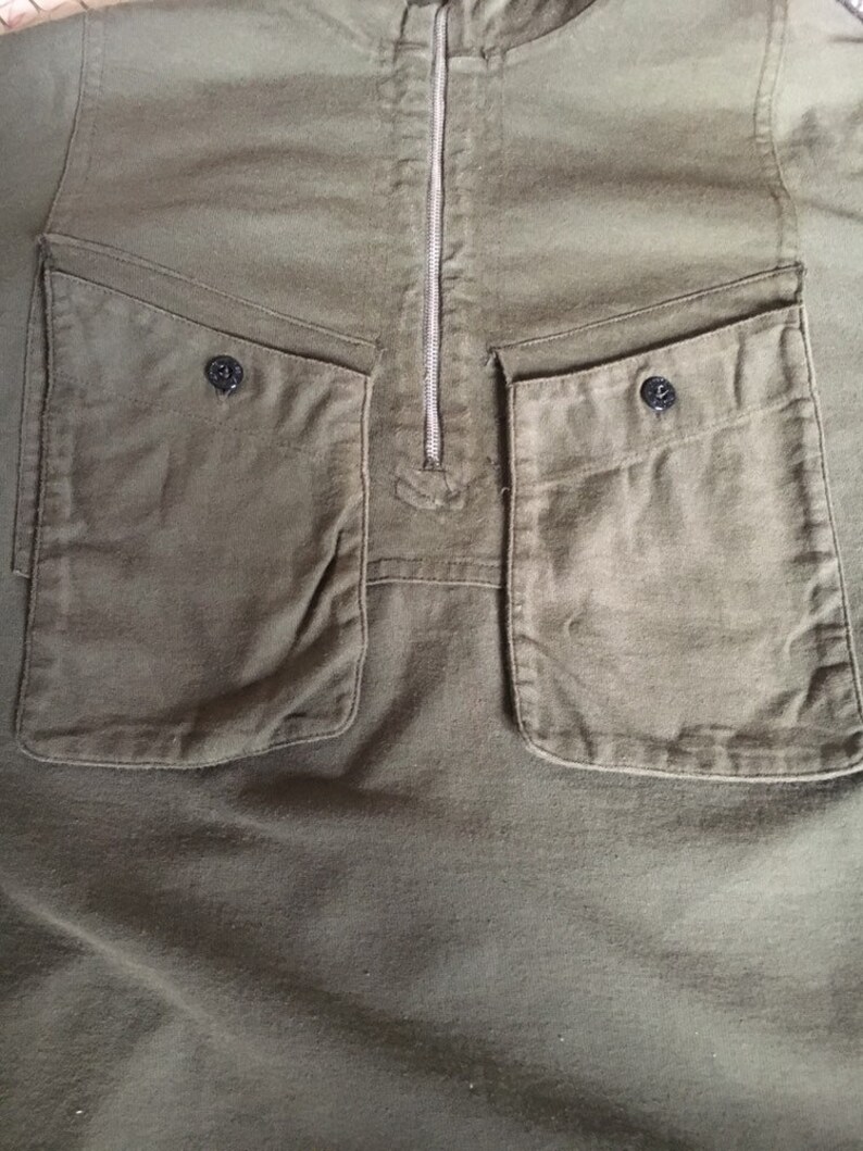 May include: A green, long-sleeved shirt with a zipper closure and two large pockets on the front. The pockets have a flap and a button closure.