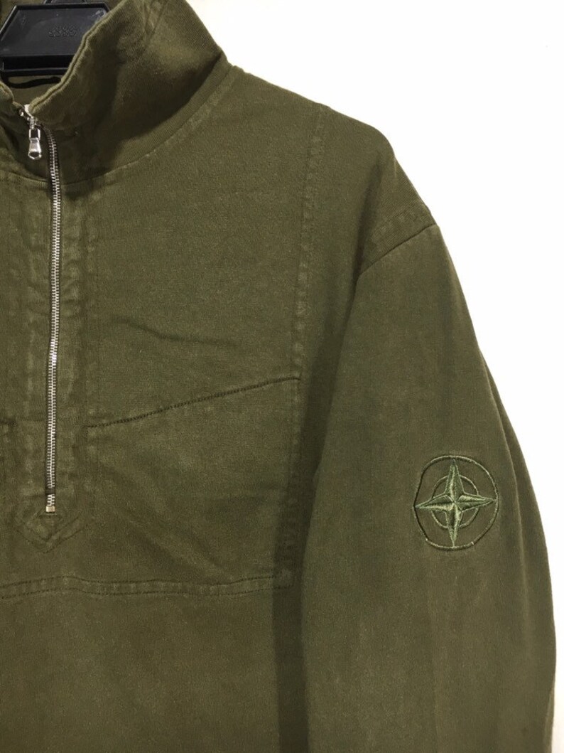 May include: A green, long-sleeved, zip-up sweatshirt with a compass logo on the left sleeve.