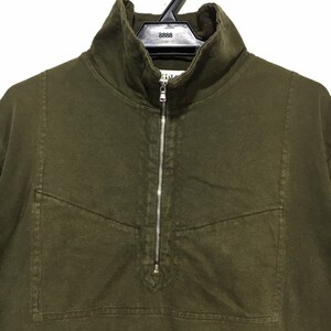 May include: A dark green, long-sleeved shirt with a zipper closure and a small pocket on the chest. The shirt has a mock neck collar.