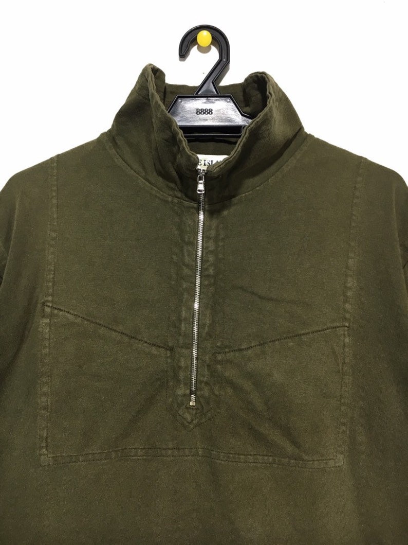 May include: A dark green, long-sleeved shirt with a zipper closure and a small pocket on the chest. The shirt has a mock neck collar.