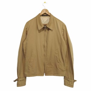 May include: A tan zip-up jacket with long sleeves and a collared neckline. The jacket has a strap detail on the cuffs.