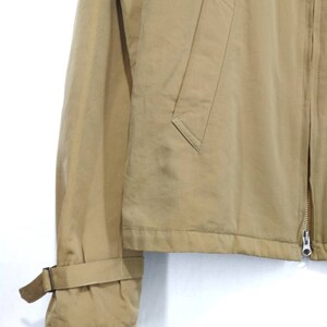 May include: A tan jacket with a zipper closure and a flap pocket on the front. The jacket has a long sleeve with a strap and buckle detail on the cuff.