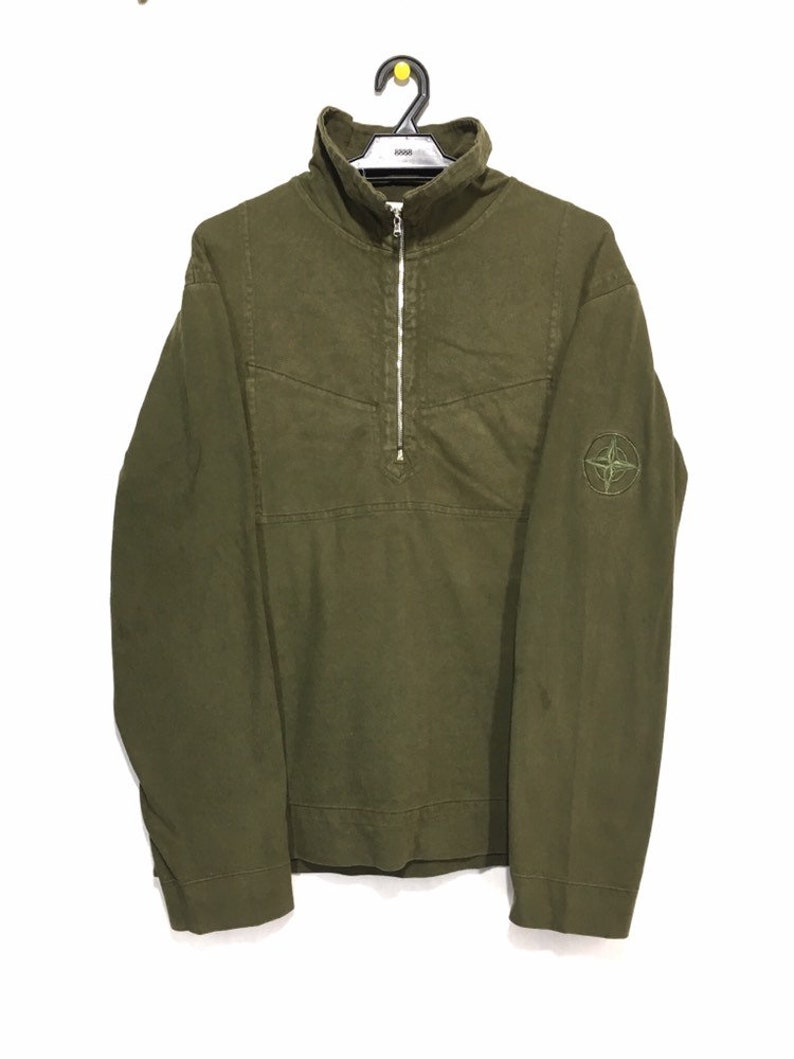 May include: A green long-sleeve shirt with a half-zip closure and a compass logo on the left sleeve.