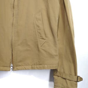 May include: A tan zip-up jacket with a flap pocket on the left side and a strap on the right sleeve.
