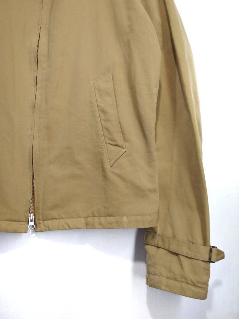 May include: A tan zip-up jacket with a flap pocket on the left side and a strap on the right sleeve.