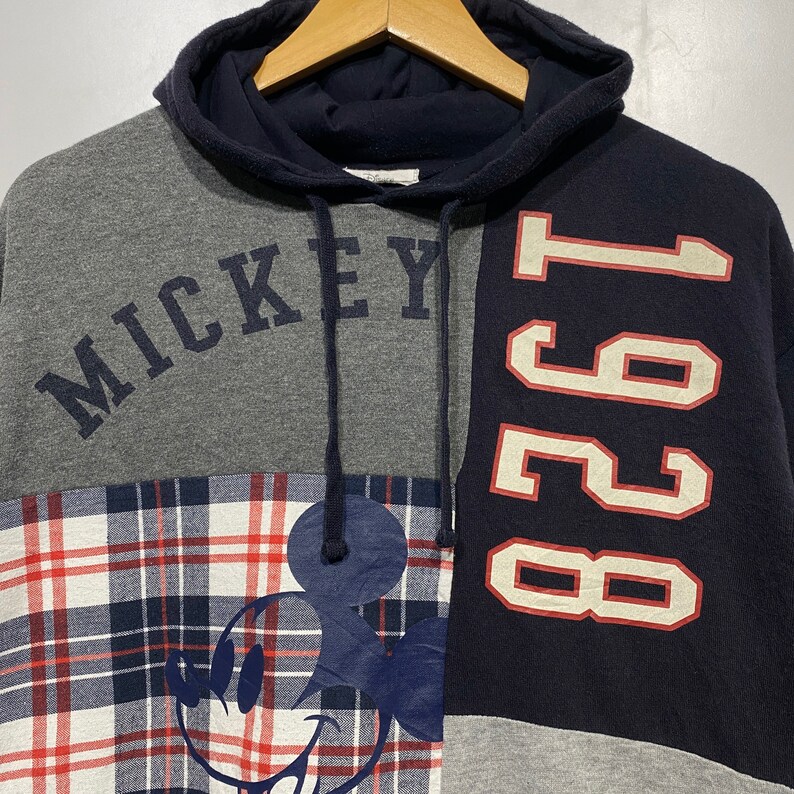 Puede incluir: Una sudadera con capucha de color gris, azul y rojo con un dise&ntilde;o de Mickey Mouse y el texto "Mickey" y "1991".