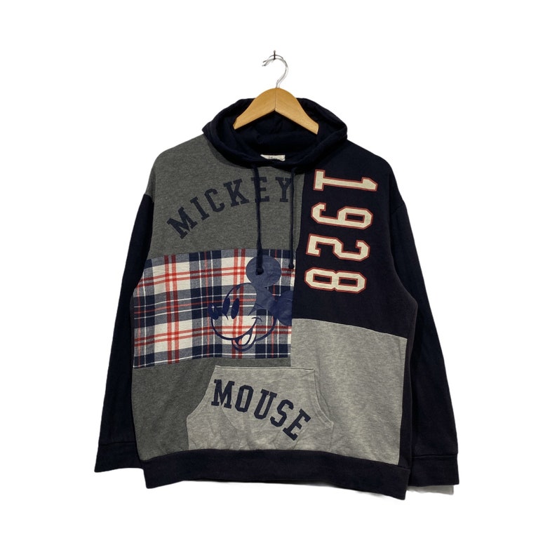 Puede incluir: Una sudadera con capucha de color azul, gris y rojo con un gr&aacute;fico de Mickey Mouse y el texto "Mickey Mouse 1928" en la parte delantera.