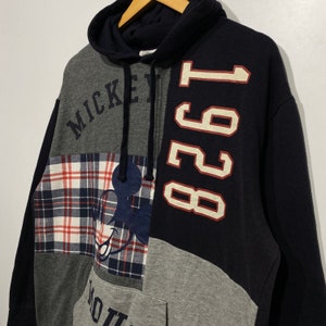 Puede incluir: Una sudadera con capucha de color negro, gris y rojo con un dise&ntilde;o de Mickey Mouse y el texto "Mickey" y "1981".