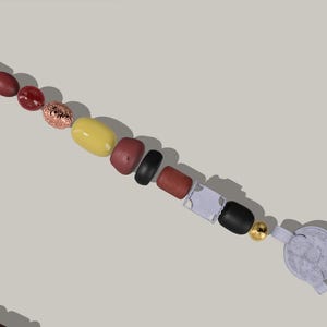 Può includere: Una lunga collana di perline con una varietà di colori e forme, tra cui marrone, rosso, giallo, nero e bianco. La collana termina con un ciondolo bianco.