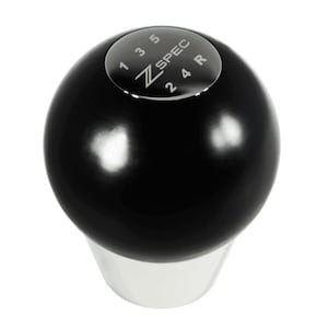 May include: A black shift knob with a silver base. The top of the knob has a silver cap with the text "Z SPEC" and gear shift pattern numbers 1, 2, 3, 4, 5, and R. The knob is a sphere shape.