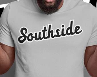 May include: A man wearing a grey t-shirt with the word "Southside" printed in black cursive lettering. He is looking at the camera with a surprised expression and has his hands raised in the air.