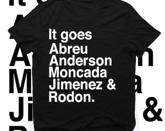 May include: Black t-shirt with white text that reads "It goes Abreu Anderson Moncada Jimenez & Rodon." The words are stacked vertically. The words "It goes" are at the top. The shirt is on a white background.