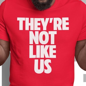 May include: Red t-shirt with white text that reads "They're Not Like Us."