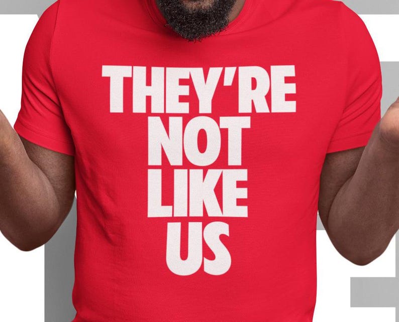 May include: Red t-shirt with white text that reads "They're Not Like Us."