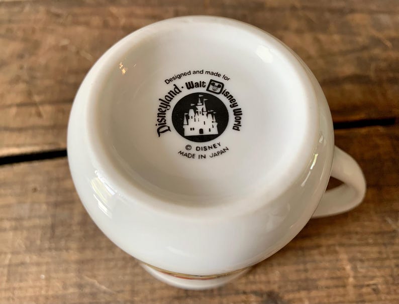 K&ouml;nnte beinhalten: Wei&szlig;e Disney-Tasse aus Keramik mit Henkel. Der Boden der Tasse zeigt die Logos von Disneyland und Walt Disney World mit dem Text "Designed and made for Disneyland Walt Disney World" und "Made in Japan".