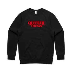 Op de afbeelding: Zwart longsleeve sweatshirt met een rode grafische print die "Queerer Things" zegt in een stijl die lijkt op de populaire show "Stranger Things".
