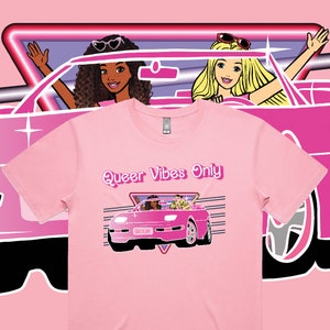 May include: Pink t-shirt with a graphic of three women driving a pink convertible with the text "Queer Vibes Only".