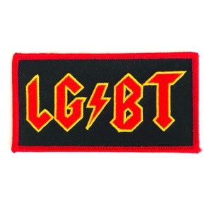 May include: A black fabric patch with a red embroidered border. The patch features the letters "LGBT" in a stylised, bold font with a lightning bolt between the "G" and "B". The letters are outlined in yellow.