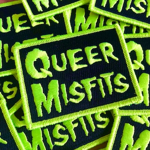 May include: Close-up of a black fabric patch with a neon green embroidered border and the text "QUEER MISFITS" in neon green.