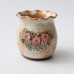 May include: A white ceramic planter with a scalloped rim and a brown glaze. The planter has a raised design of leaves and pink flowers.