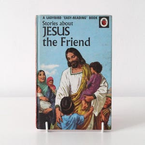 May include: A vintage Ladybird Easy-Reading book titled Stories about Jesus the Friend. The light blue cover features a colour illustration of a bearded figure in a white robe and yellow sash interacting with several children and a woman.