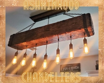 Op de afbeelding: Een rustieke houten kroonluchter met zes Edison-lampjes die hangen aan een gerecycled houten balk. De kroonluchter is aan het plafond gehangen met een ketting en heeft een eenvoudig, industrieel ontwerp.