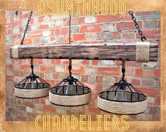 May include: A rustic wooden chandelier with three black metal cage light fixtures and natural rope accents. The chandelier is hanging from a chain against a brick wall. The text "ASHMINWOOD CHANDELIERS" is visible below the chandelier.