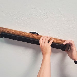 May include: A person is installing a black metal light fixture with a wooden base on a white wall.