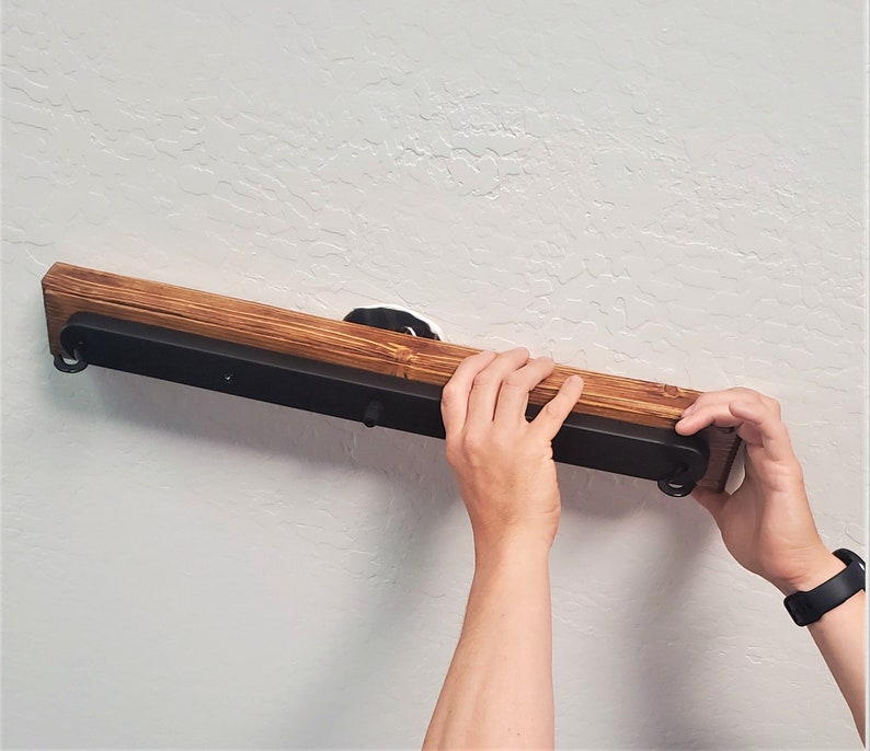 May include: A person is installing a black metal light fixture with a wooden base on a white wall.