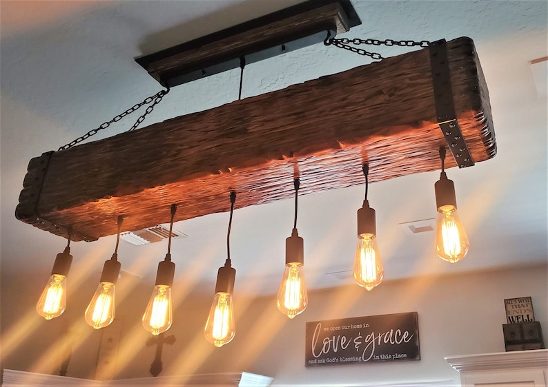 May include: A rustic wooden beam chandelier with six Edison bulb lights hanging from black cords. The beam is stained a dark brown and has metal accents. The chandelier is hanging from a chain.
