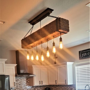May include: A rustic wooden beam chandelier with six Edison bulb lights hanging from black cords. The chandelier is suspended from the ceiling with black chains.