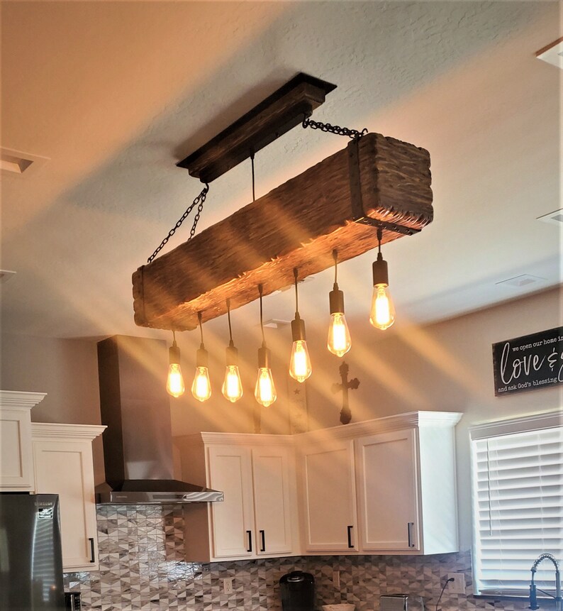 May include: A rustic wooden beam chandelier with six Edison bulb lights hanging from black cords. The chandelier is suspended from the ceiling with black chains.
